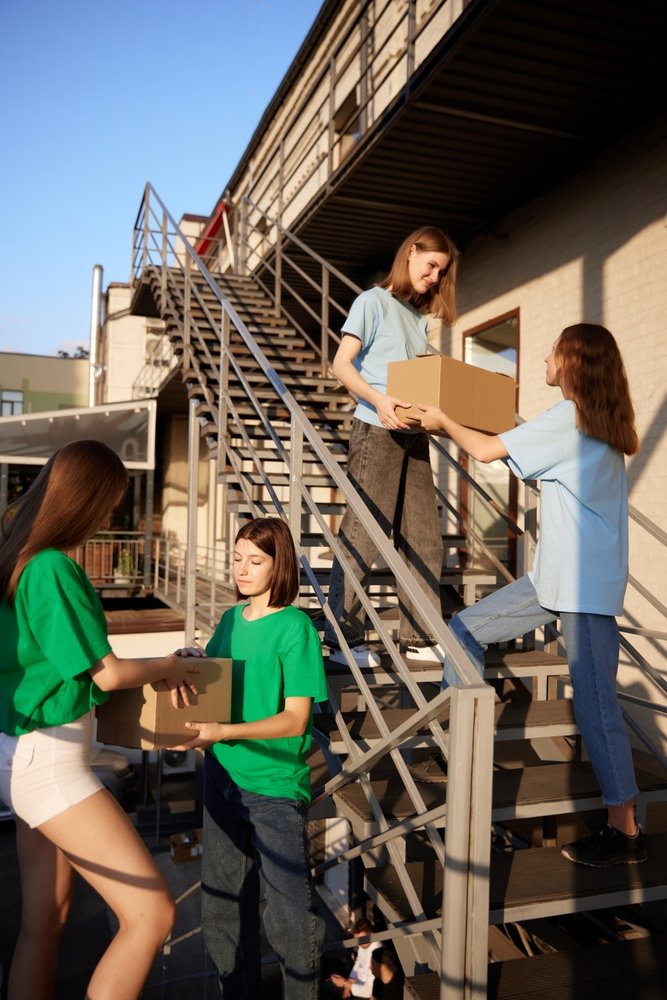 Girls,,Volunteers,Standing,On,Stairs,With,Boxes,Filled,With,Humanitarian