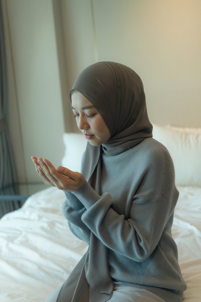 Young,Woman,Wearing,A,Hijab,Sits,On,A,Bed,With